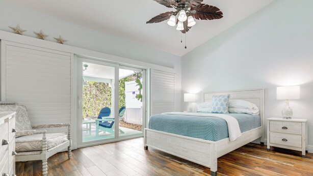 Quarto com cama, poltrona, mesa de cabeceira e ventilador de teto.