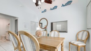 Uma sala de jantar com mesa e cadeiras de madeira, um espelho redondo e arte decorativa de peixes na parede.