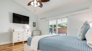 Quarto com cama, penteadeira branca e televisão na parede.