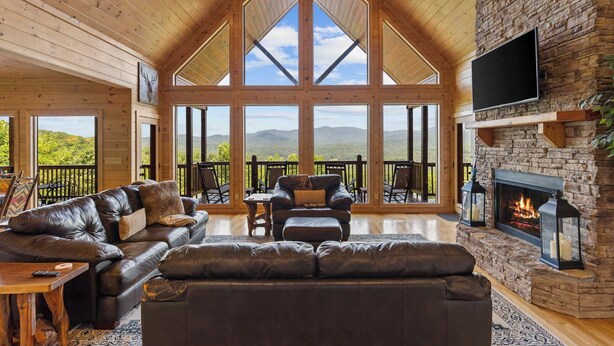 Un salon spacieux doté d’une cheminée en pierre, de canapés en cuir et de grandes fenêtres offrant une vue sur les montagnes.