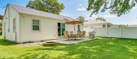 A single-story house with a patio area featuring a table and chairs, a grill, and a covered seating area.