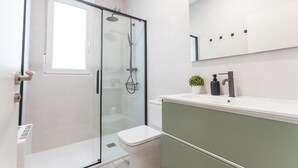 Ein modernes Badezimmer mit Duschkabine aus Glas, einer weißen Toilette und einem grünen Waschtisch mit Waschbecken und Spiegel.