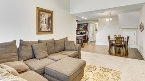 Ein Wohnzimmer mit einem Ecksofa, einem Deckenventilator, einer Küche im Hintergrund und einem Essbereich mit Holztischen und -stühlen.