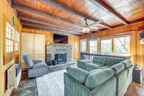 A cozy cabin interior with a stone fireplace, wooden walls, and a large green sofa. - Between Big Bear & Lake Arrowhead - Cabin w/ View! (Running Springs)
