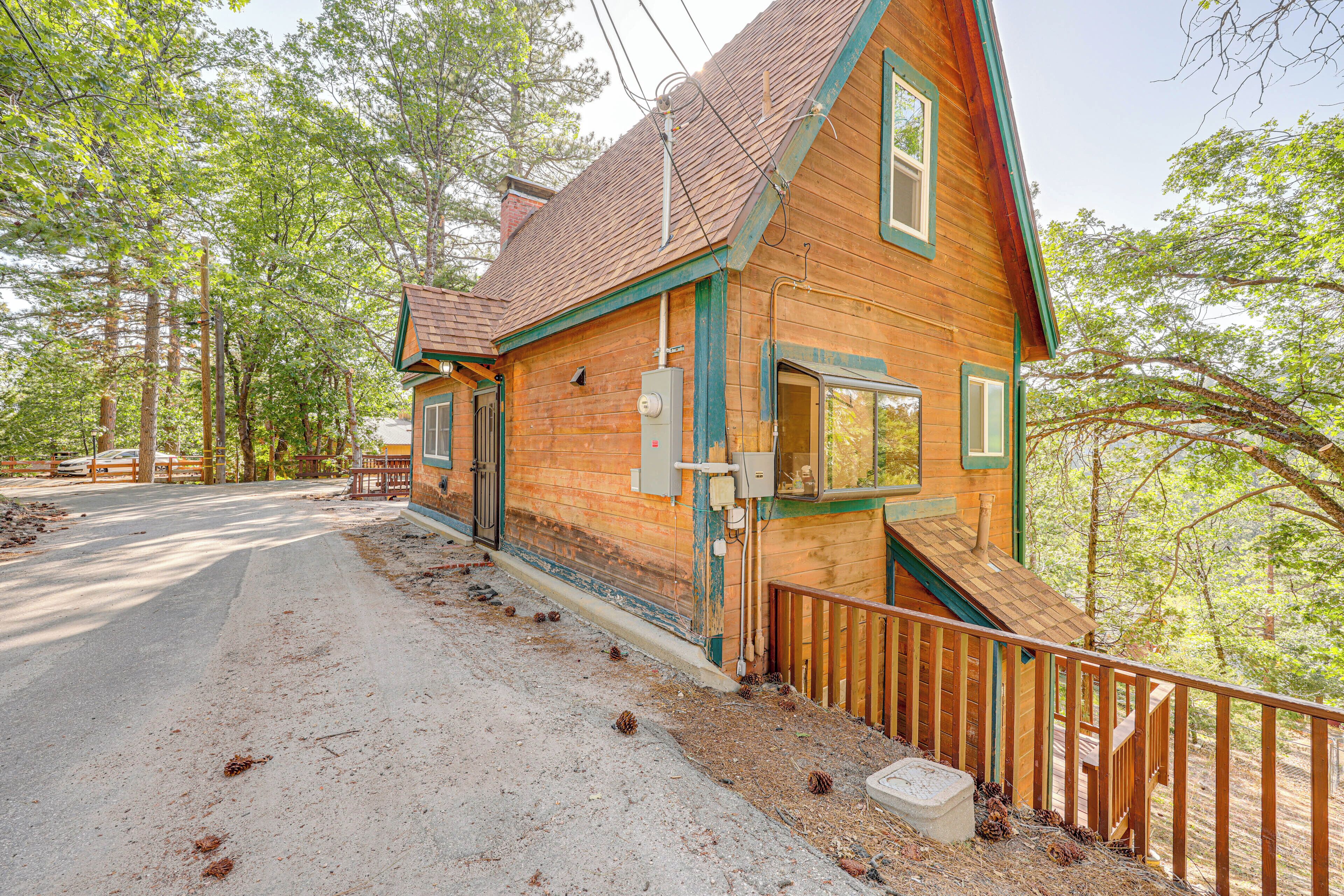 Une cabane en bois rustique, dotée d’une véranda, d’une allée en terre et bordée par une forêt.