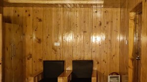 A wooden cabin with two black chairs and a small heater. - Harsil apple homestay (Bhatwari)