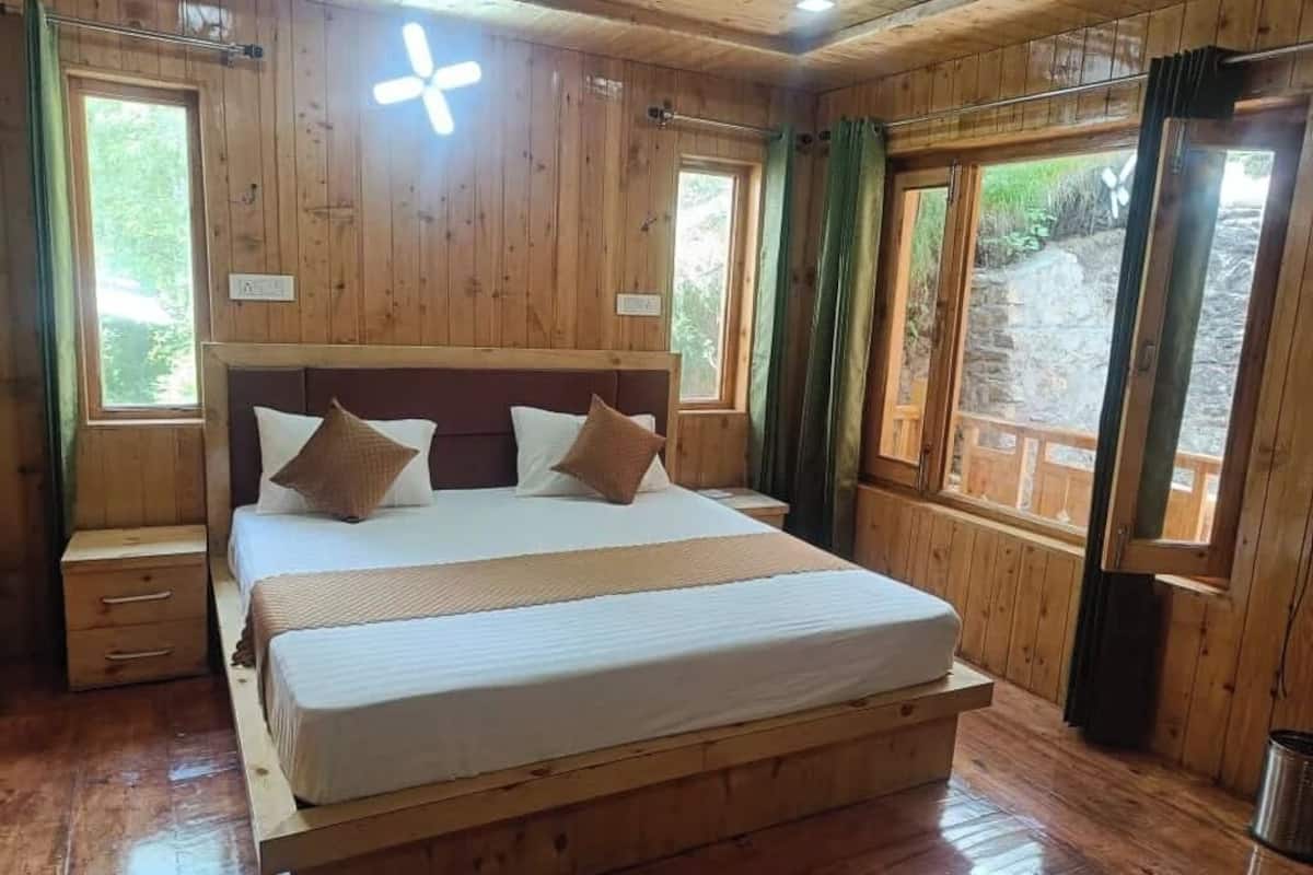 A wooden bedroom with a large bed, two bedside tables, and a window with curtains.