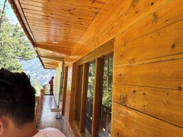 A wooden corridor with large windows and a balcony overlooking a mountainous landscape.