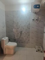 A small bathroom with a toilet, a shower, and a water heater mounted on the wall.