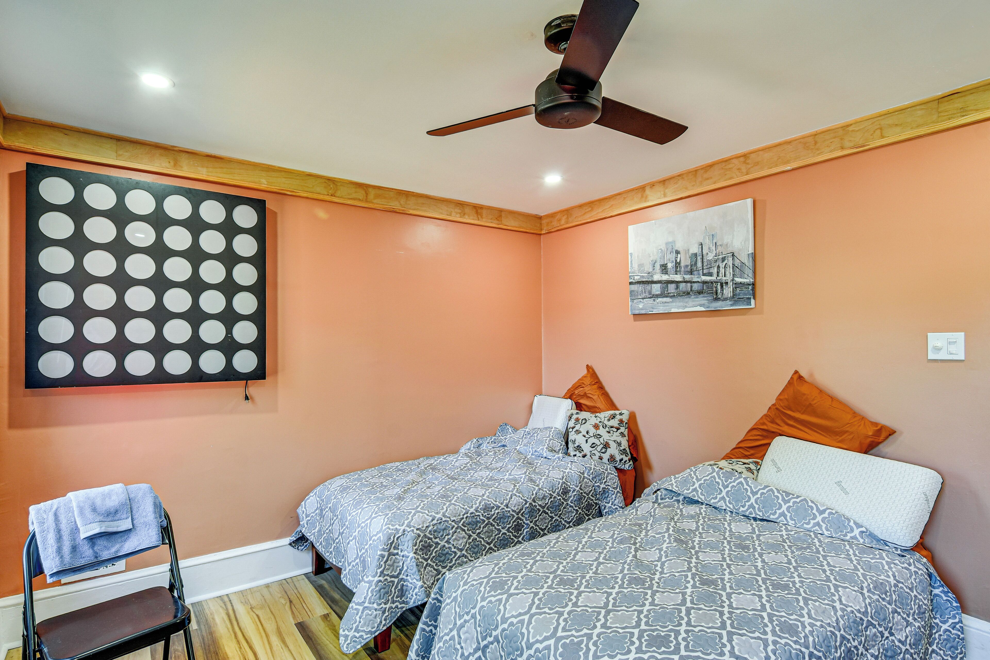 A bedroom with two beds, a ceiling fan, a chair, and artwork on the walls.