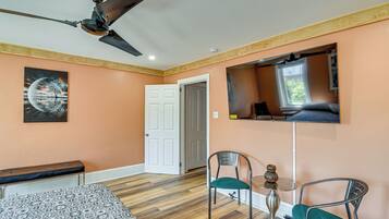 A bedroom with a ceiling fan, a bed, a bench, two chairs, a small table, and a TV mounted on the wall.