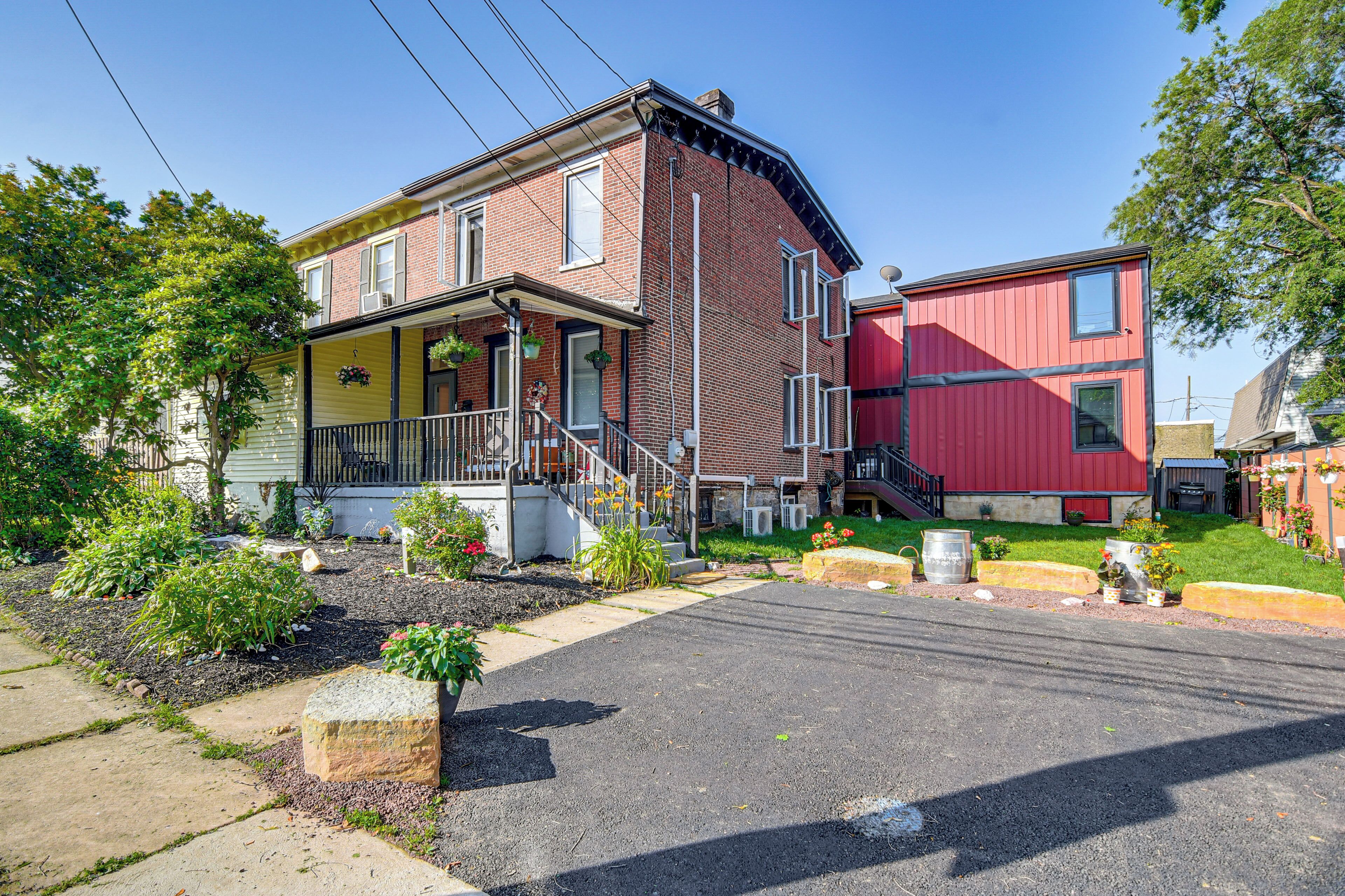 A two-story house with a porch, a red exterior, and a small front yard with plants and a stone planter.