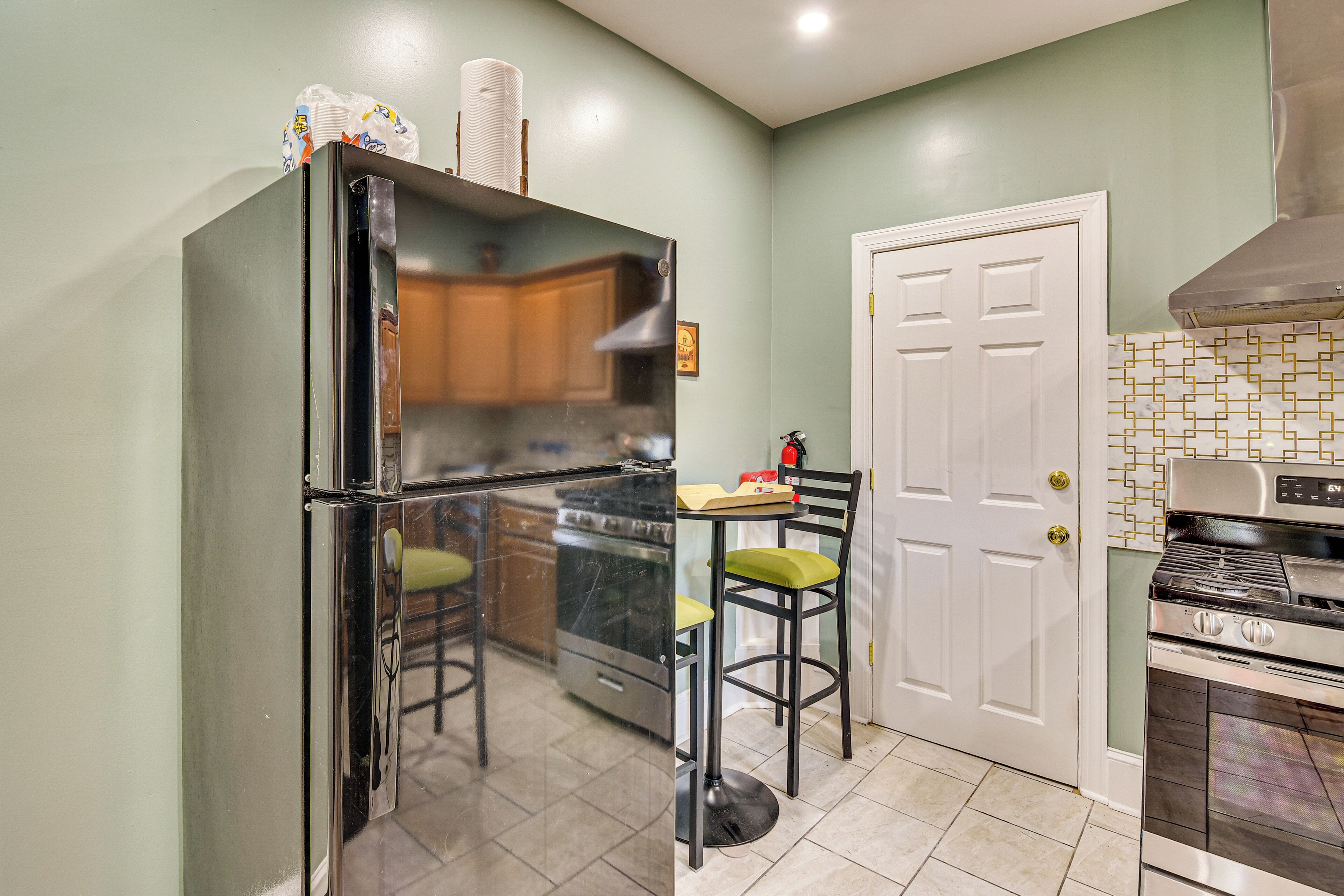 Una cocina con refrigerador, estufa y horno. Se aprecia una puerta con marco blanco y un salpicadero de azulejos decorativos.