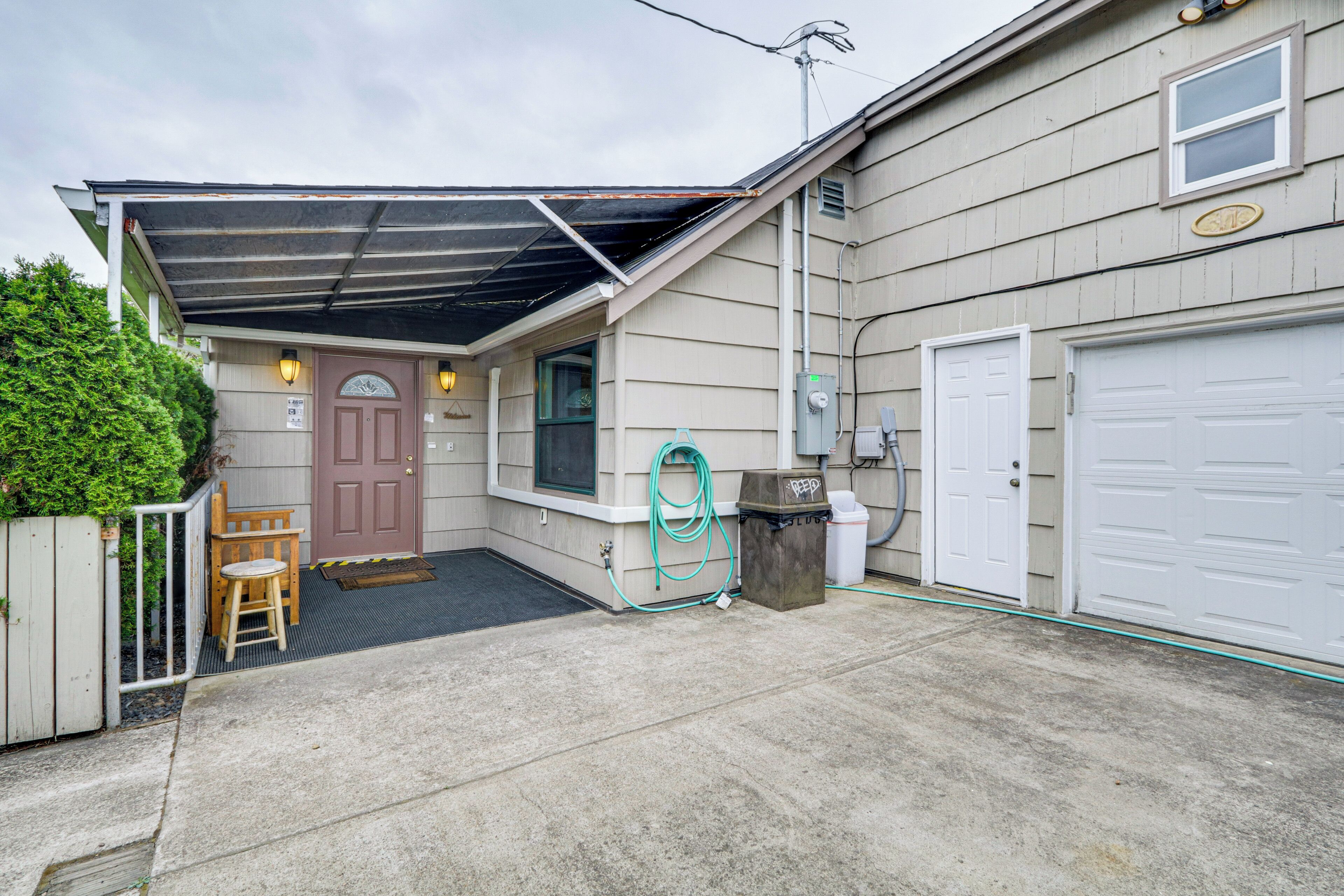 A residential garage with a covered entryway, a wooden chair, and a hose.