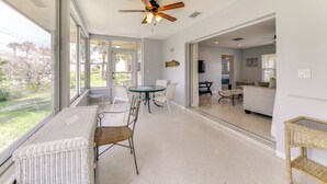 A spacious room with a large window, a ceiling fan, a dining area with a table and chairs, and a wicker bench. - 30-Day Retreat Near Siesta Key | Pet Friendly (Sarasota)