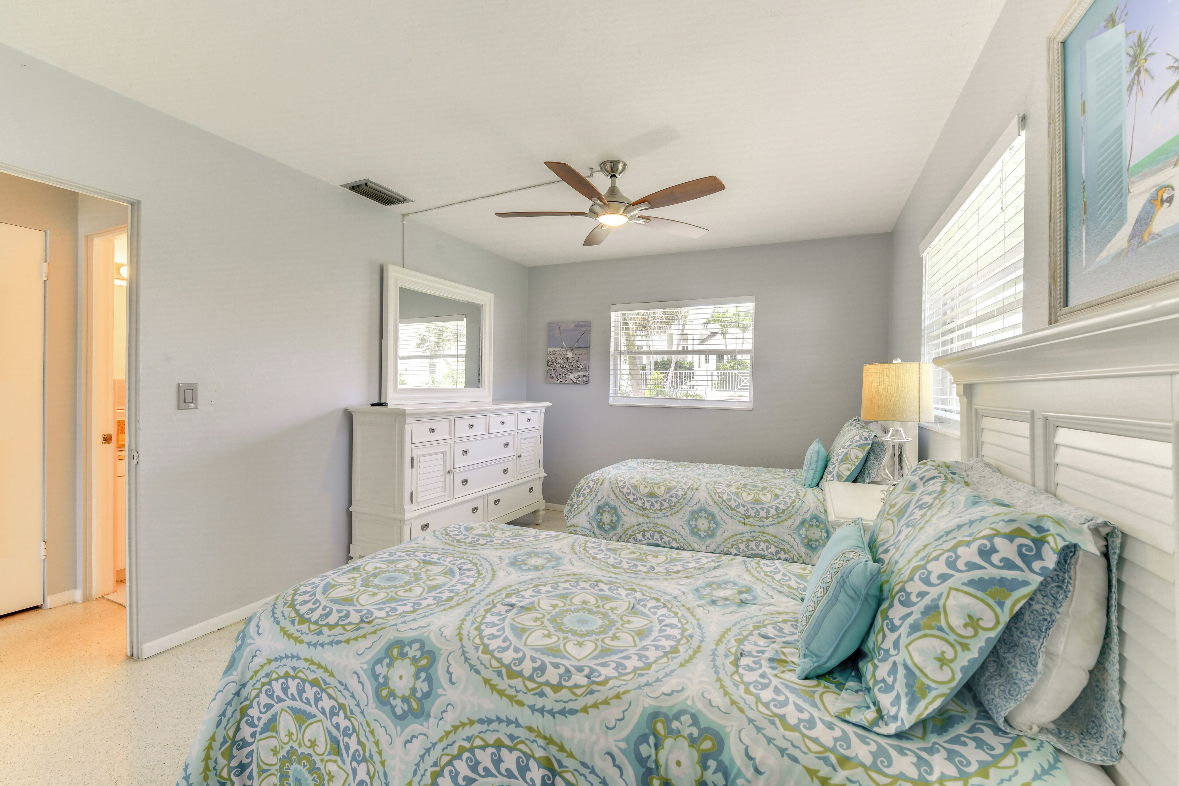 A bedroom with two beds, a ceiling fan, a dresser, and a window with blinds.