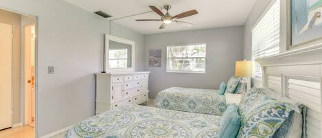 A bedroom with two beds, a ceiling fan, a dresser, and a window with blinds.