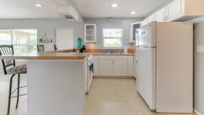 A kitchen with white cabinets, a refrigerator, a sink, and a window with blinds. - 30-Day Retreat Near Siesta Key | Pet Friendly (Sarasota)