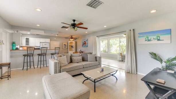 A spacious living area with a sofa, coffee table, and chairs. A kitchen with white cabinets and a dining area with bar stools is visible. - 30-Day Retreat Near Siesta Key | Pet Friendly (Sarasota)