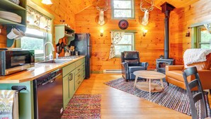 A cozy cabin interior with wooden walls, a kitchen with modern appliances, a fireplace, and a dining area. - On 30 Acres w/ Trails & Garden: Stockholm Cabin! (Stockholm)