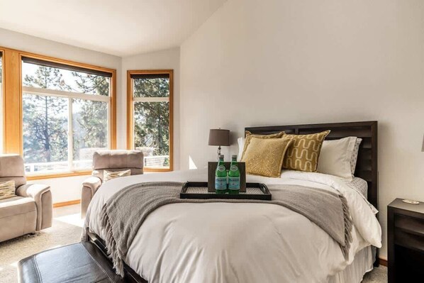 A bedroom with a large bed, a nightstand, a chair, and two windows. - Lakeside Family Retreat with Breathtaking Views (Coeur d'Alene)