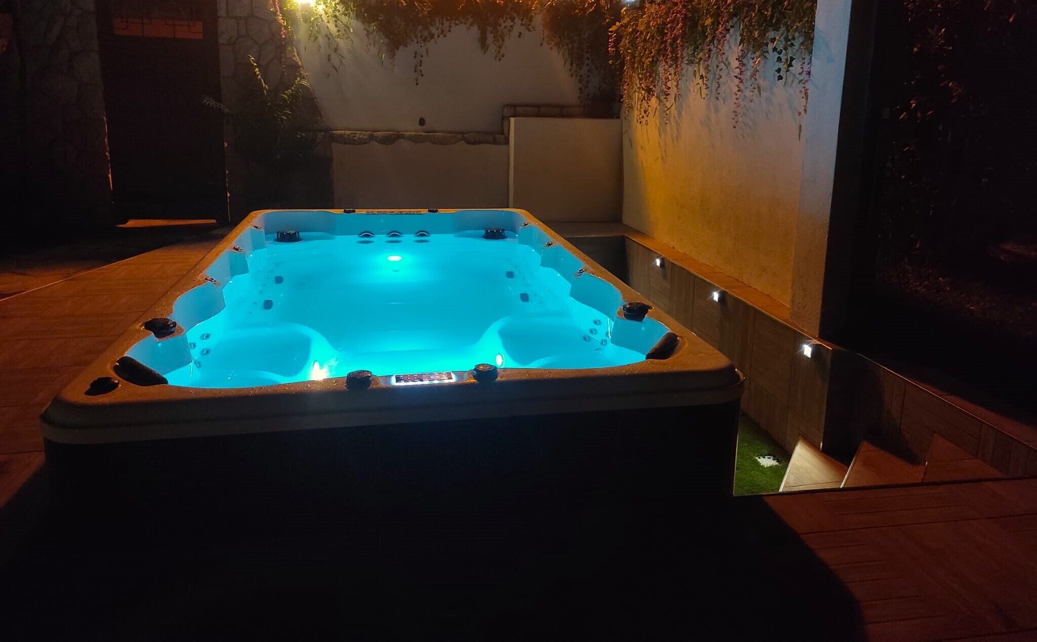 Un bain à remous avec un éclairage bleu, entouré d’un mur de pierres et d’une terrasse en bois.