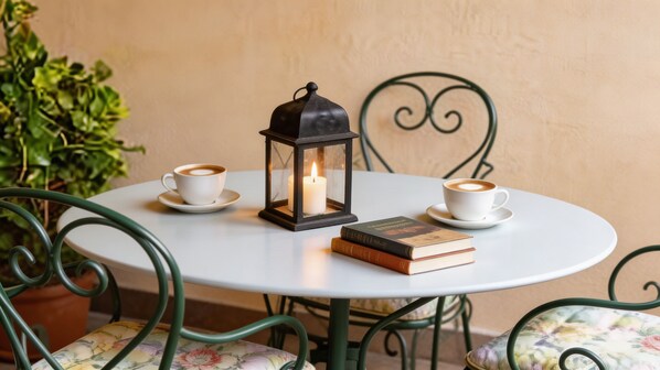 A round table with two white cups of coffee, a lit candle in a lantern, and a stack of books.