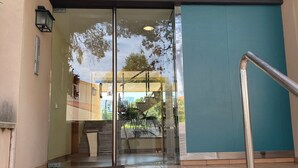 Entrada de un edificio con puerta de vidrio, barandilla de metal y piso de baldosas.
