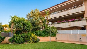 Un immeuble résidentiel à plusieurs étages, doté de balcons, d’un jardin bien entretenu et offrant une vue sur un ciel dégagé.