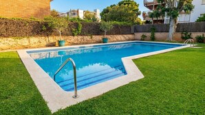 Una piscina rectangular con una escalera de metal, rodeada de césped cuidado y un muro de piedra con plantas.
