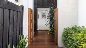 Un sentier bordé d’une clôture en bois qui mène à une porte surmontée d’un paillasson.
