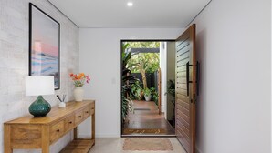 Un couloir avec une console en bois, un tableau encadré, un vase de fleurs et une porte donnant sur un jardin.