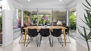 Un espace de restauration moderne avec une table en bois et des chaises noires, de grandes fenêtres et une vue sur la verdure environnante.