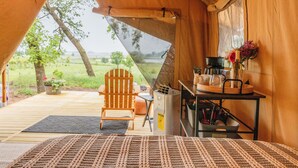 Een tent met een houten interieur, een tafel met een fles en bloemen, en uitzicht op de natuur.