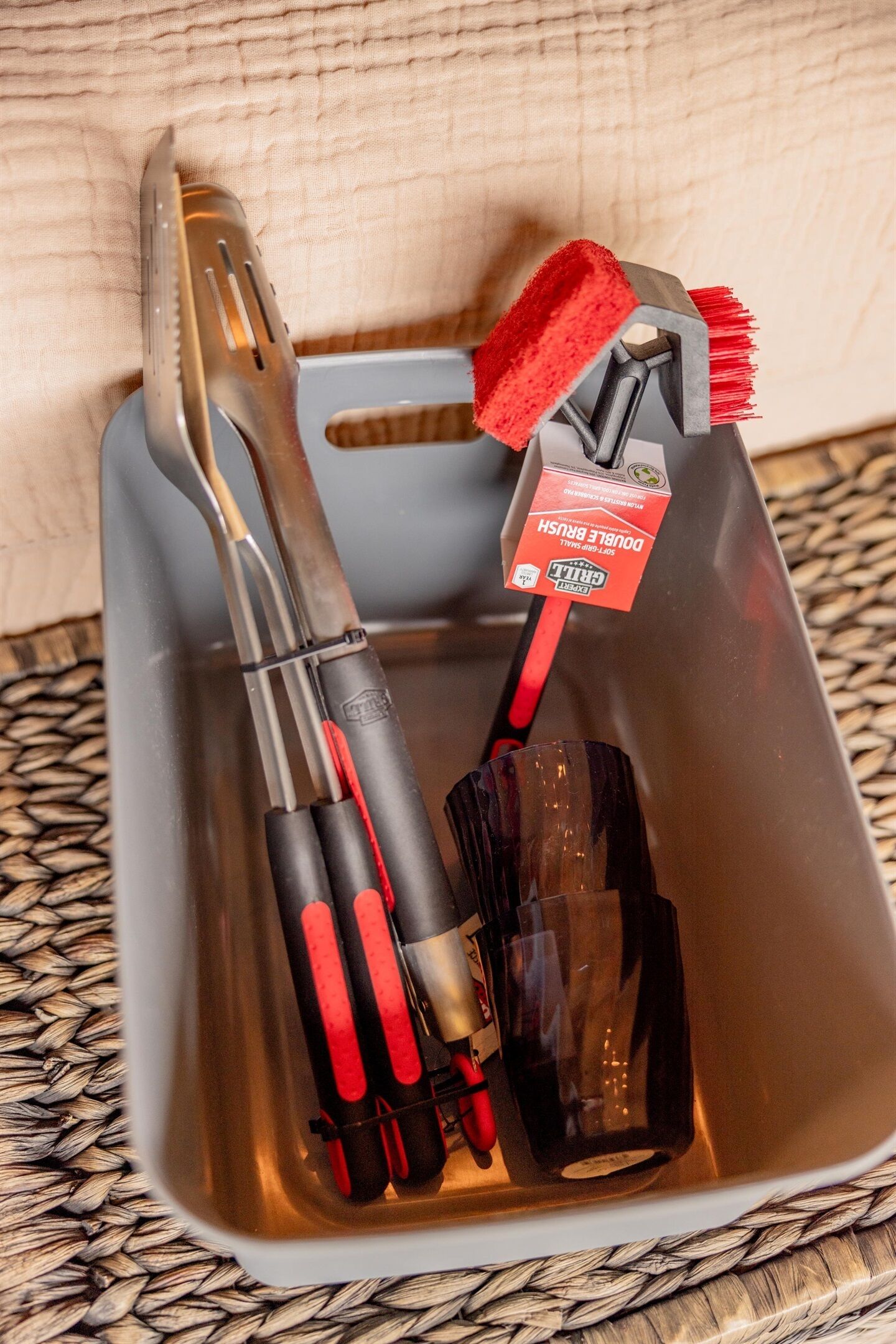 Um recipiente de plástico cinzento com várias ferramentas, incluindo alicates, uma escova e uma garrafa.