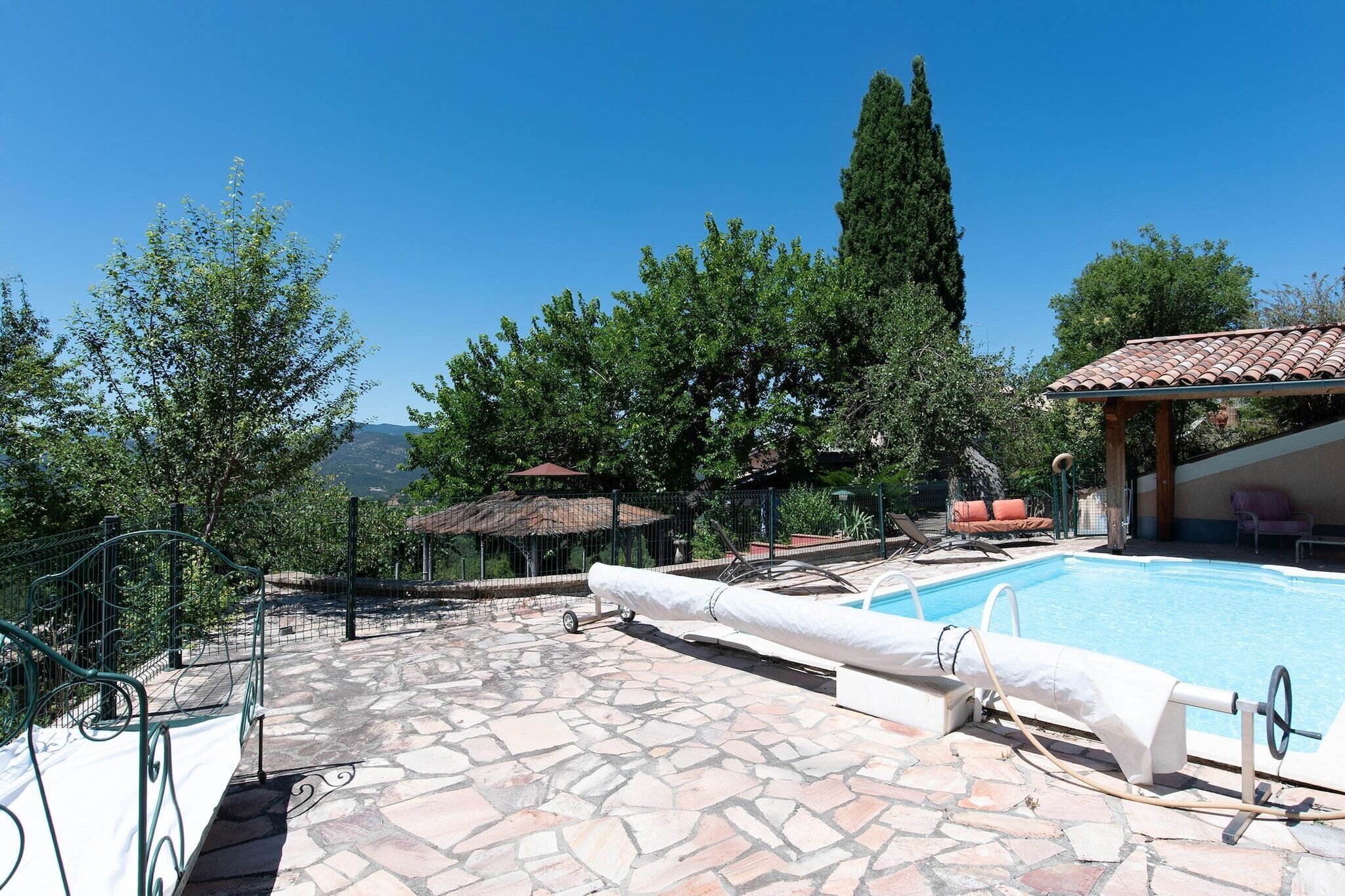 A pool area with stone flooring, lounge chairs, and a pergola.