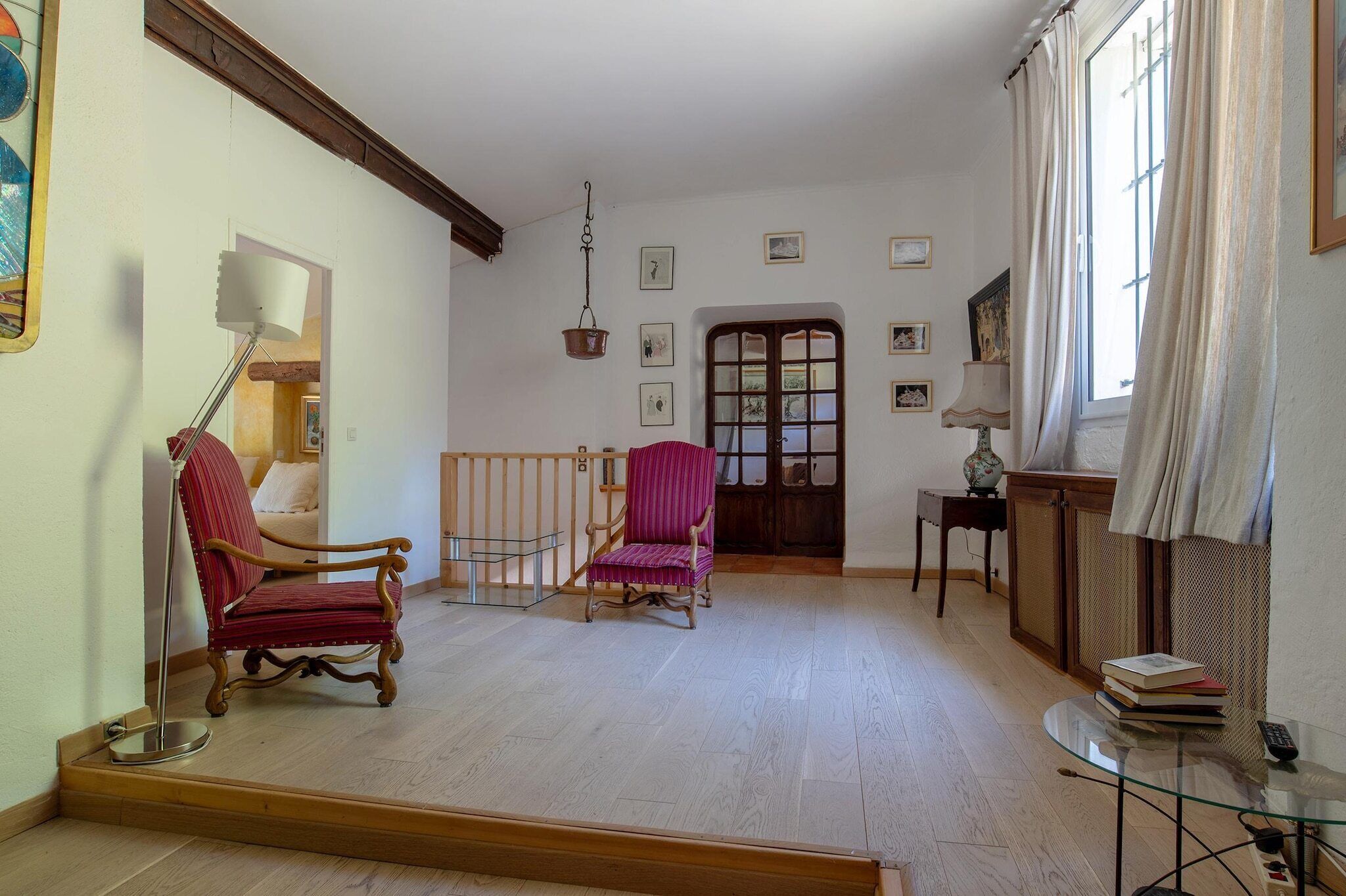 A room with a wooden floor, a red chair, a wooden cabinet, and a window with curtains.