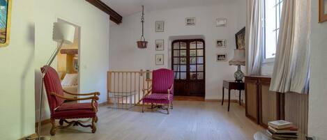 A room with a wooden floor, a red chair, a wooden cabinet, and a window with curtains.