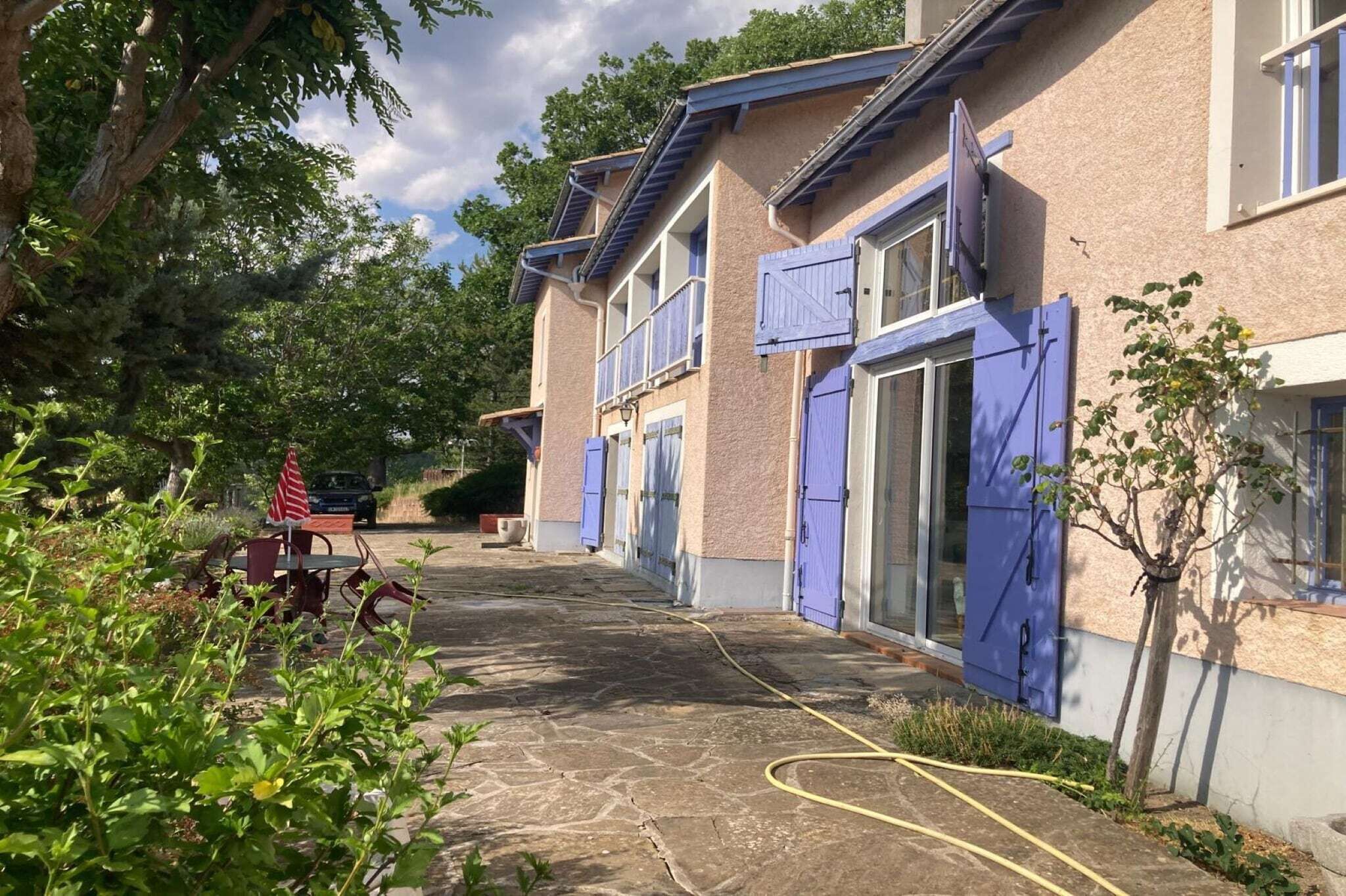 Ein Gebäude mit einem Steinweg, blauen Fensterläden und einem Garten mit Tisch und Stühlen.