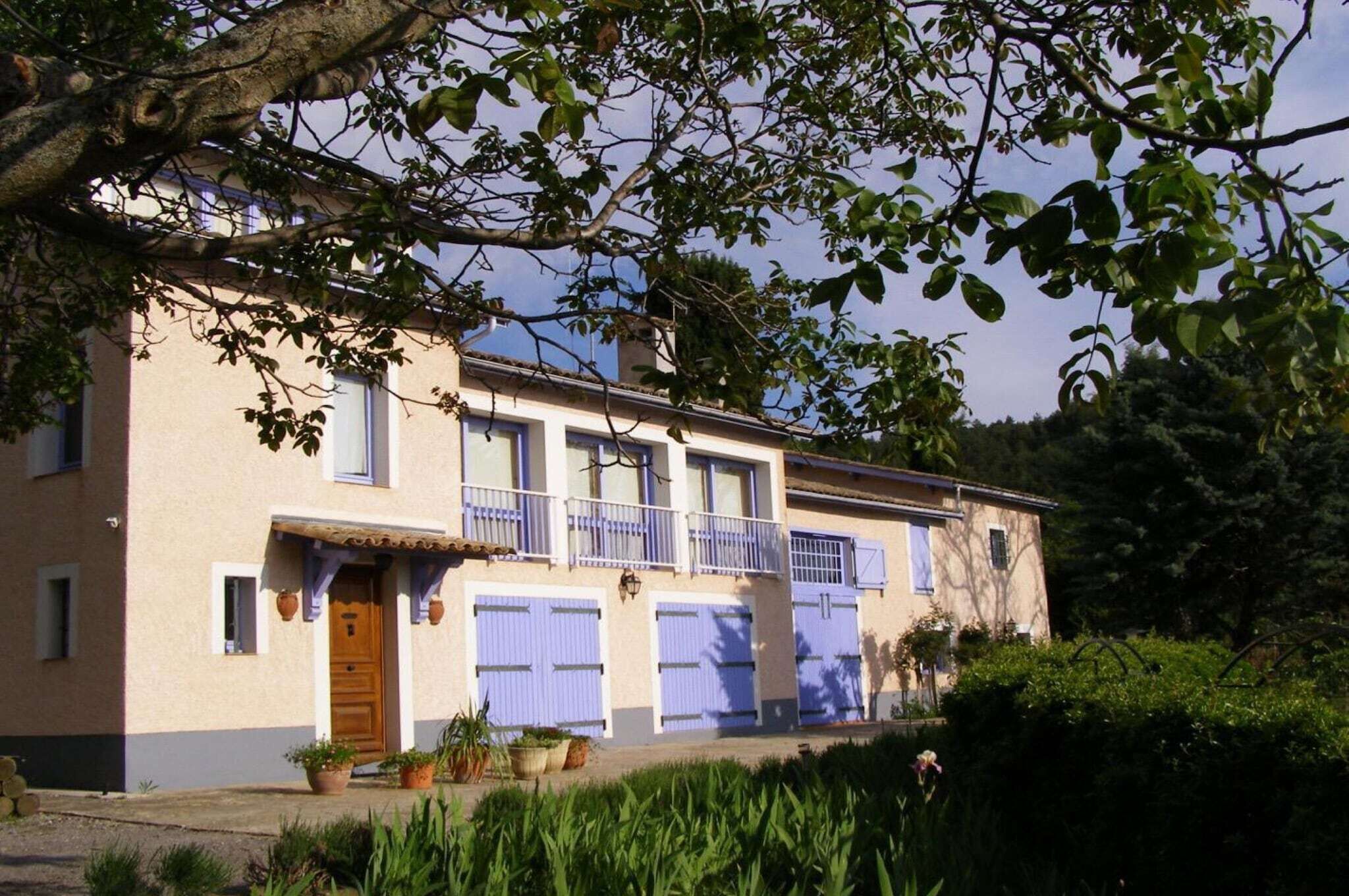 A two-story building with a balcony, a wooden door, and a garden area with potted plants.