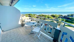 A balcony with a view of the sea, a small table, and two white chairs.
