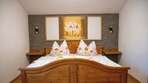 Un lit en bois avec une couvre-lit à motifs floraux et des oreillers, un mur en pierre orné d’un tableau encadré, et deux tables de chevet.