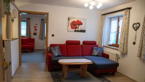Un salon avec un canapé rouge, une petite table en bois et un tableau représentant des fleurs rouges accroché au mur.