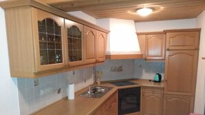 A kitchen with wooden cabinets, a sink, a stove, and a kettle. - Vacation apartment Alpenblume (Berchtesgaden)