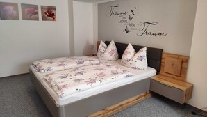 A bedroom with a bed, a nightstand, and a wall with a decorative phrase. - Vacation apartment Alpenblume (Berchtesgaden)