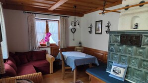 A cozy room with a wooden ceiling, a dining table with a blue tablecloth, a sofa, a wicker chair, and a bench. - Vacation apartment Alpenblume (Berchtesgaden)