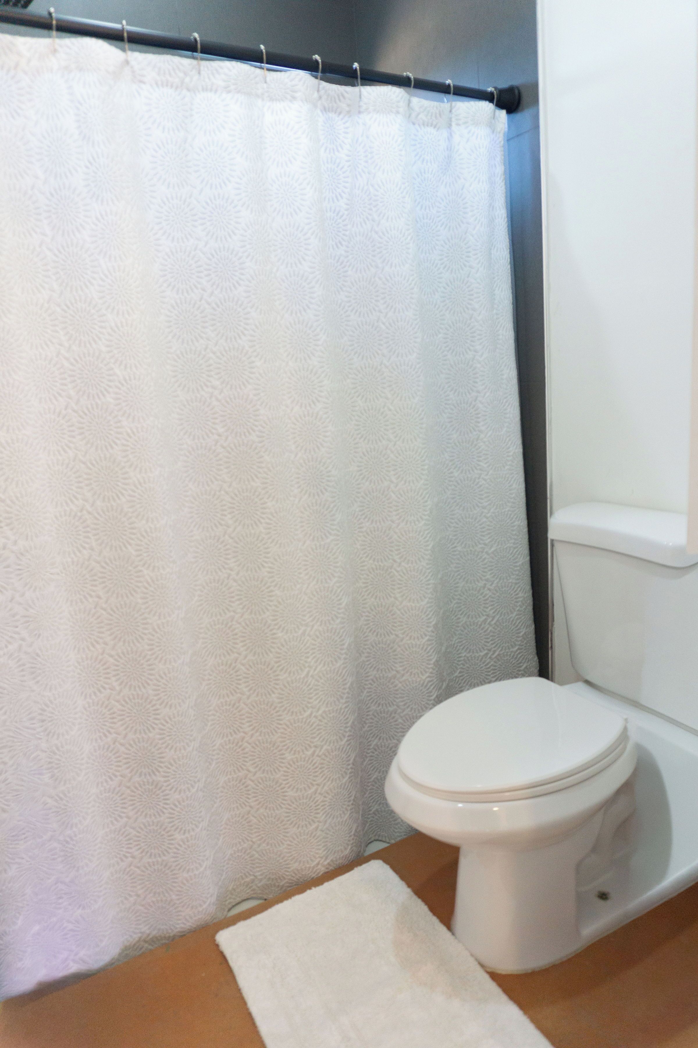 A bathroom with a white toilet, a white shower curtain, and a white bath mat.