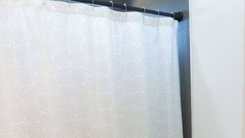A bathroom with a white toilet, a white shower curtain, and a white bath mat.