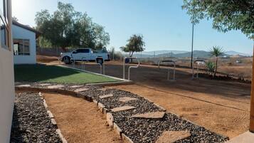 A parking area with a white pickup truck, a paved walkway with stepping stones, and a dirt path leading to a grassy area.