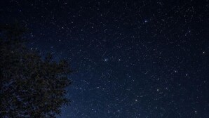 Un edificio de dos pisos con techo de tejas, un porche cubierto con sillas y un cielo nocturno estrellado.